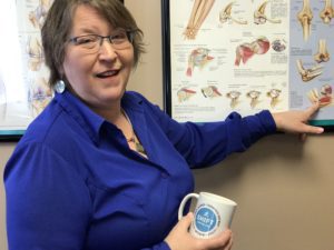 Tammy pointing to framed skeletal graphic holding SHIFT branded coffee cup smiling at camera