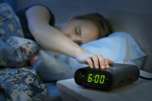 Young woman pressing snooze button on early morning digital alarm clock radio