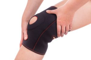 sports injuries and muscle strain of knee - person holding knee under fabric brace